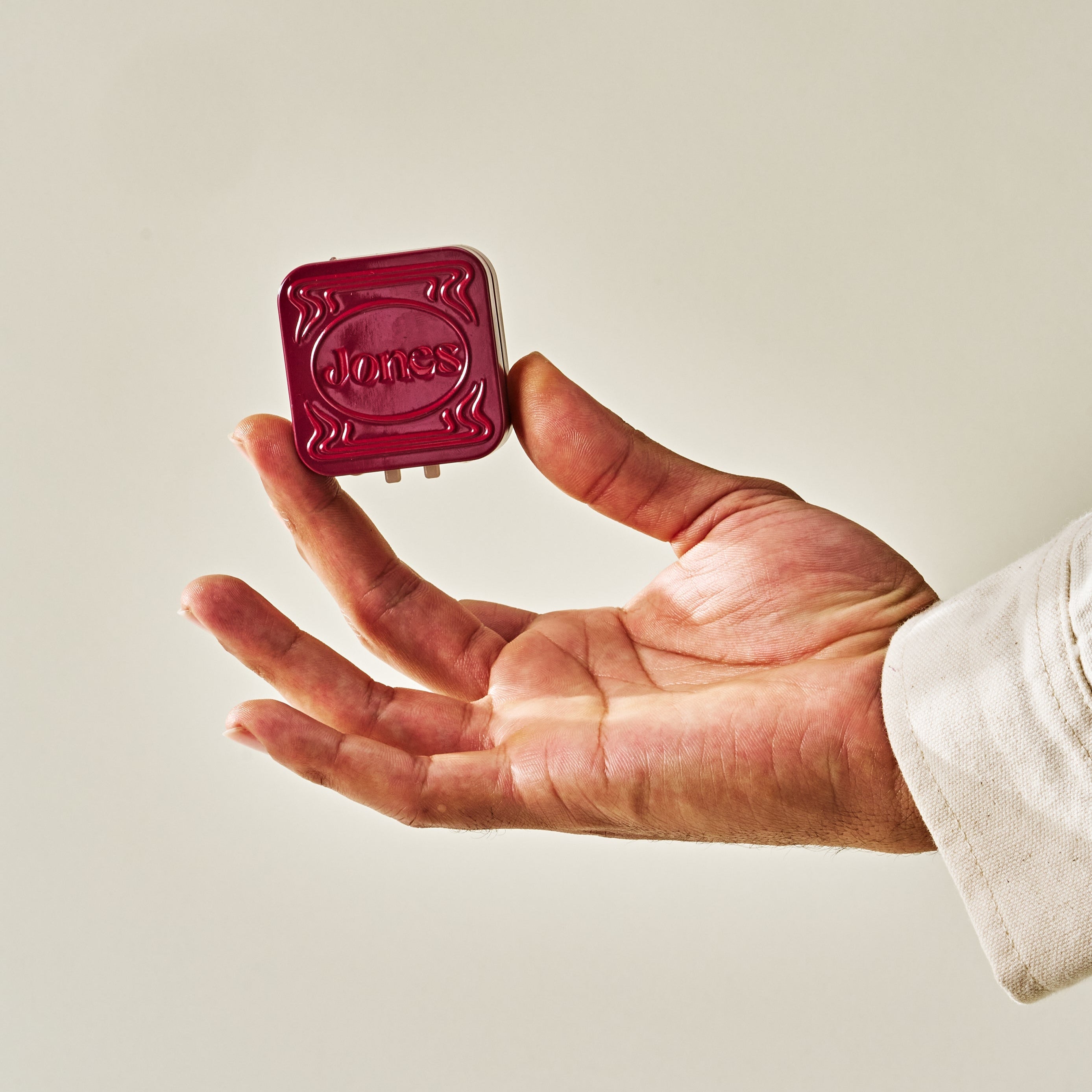 A hand holding a red embellished Jones tin holding FDA-approved mini nicotine replacement therapy lozenges in cherry flavor. The tin is child proof and says Jones on the front.