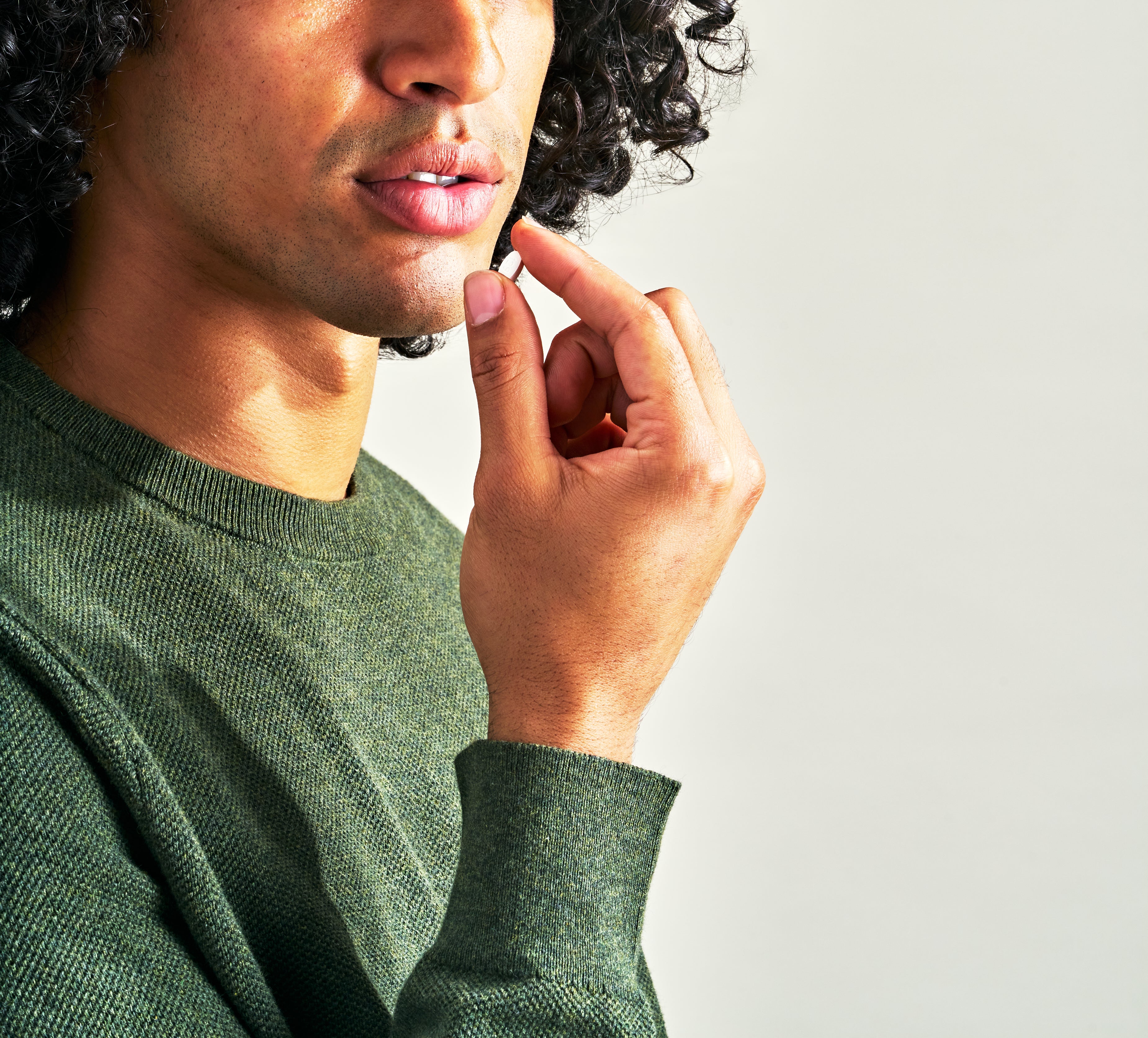 A man in a green sweater with curly dark hair taking a mini nicotine replacement therapy lozenge in mint flavor by Quit With Jones.