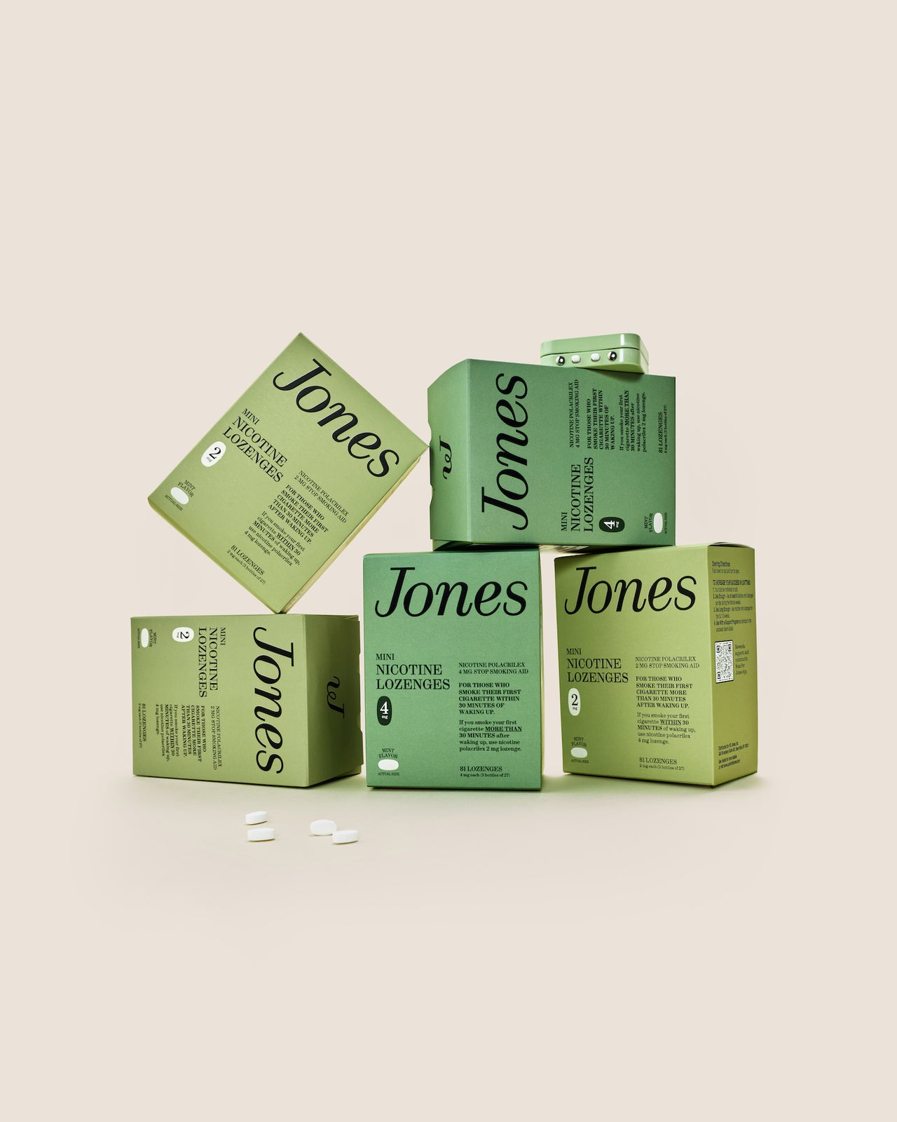 Five green boxes labeled "Jones Habit Kicker" are stacked geometrically on a beige background. Three white lozenges, part of this nicotine quit kit, are displayed in front. The boxes have minimalist text and icons.