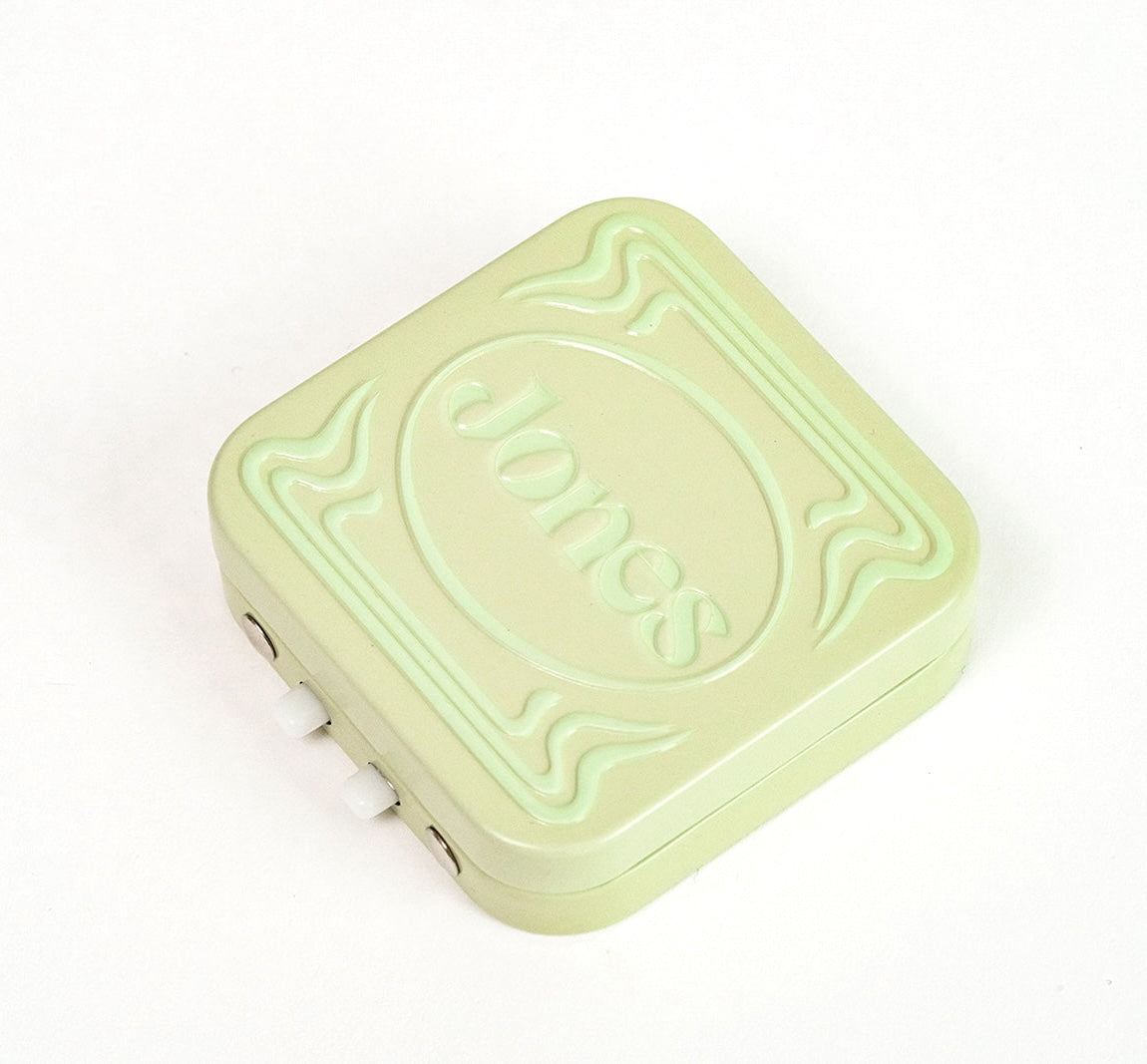 The Quit with Jones brand presents the Jones Travel Tin—a discreet, light green, square-shaped plastic mint tin embossed with "Jones," ideal for travel.