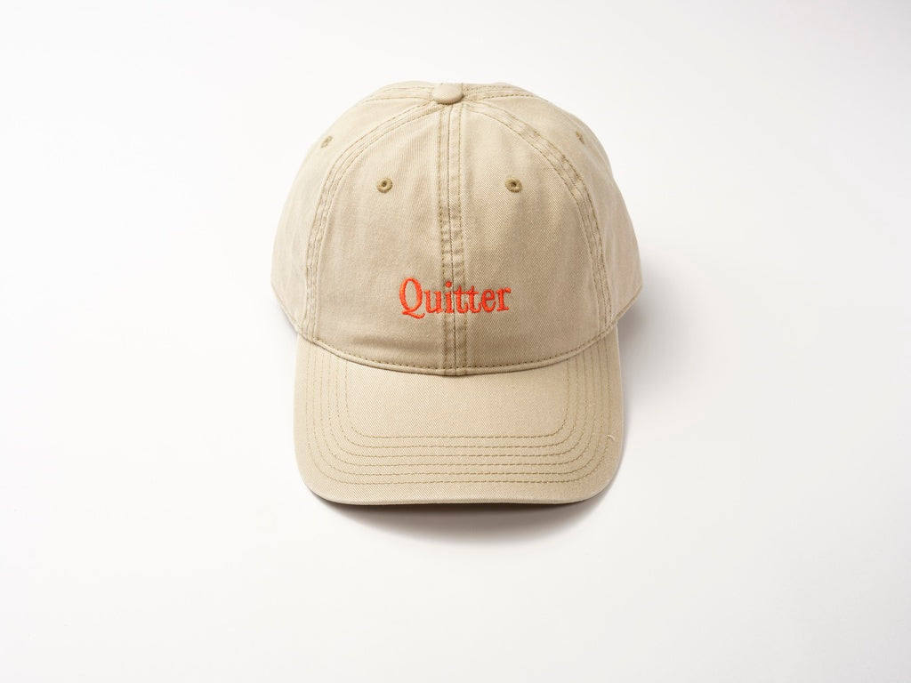 The Quitter Cap by Quit with Jones is a retro beige cotton twill baseball cap with bold red "Quitter" embroidery on the front, shown against a plain white background.