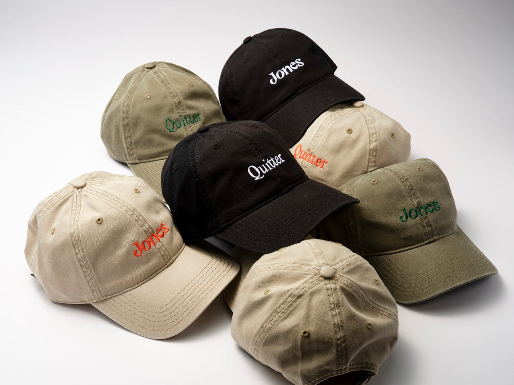 The Jones Cap by Quit with Jones is a black cotton twill baseball hat featuring "Jones" embroidered in white on the front, displayed on a white surface.