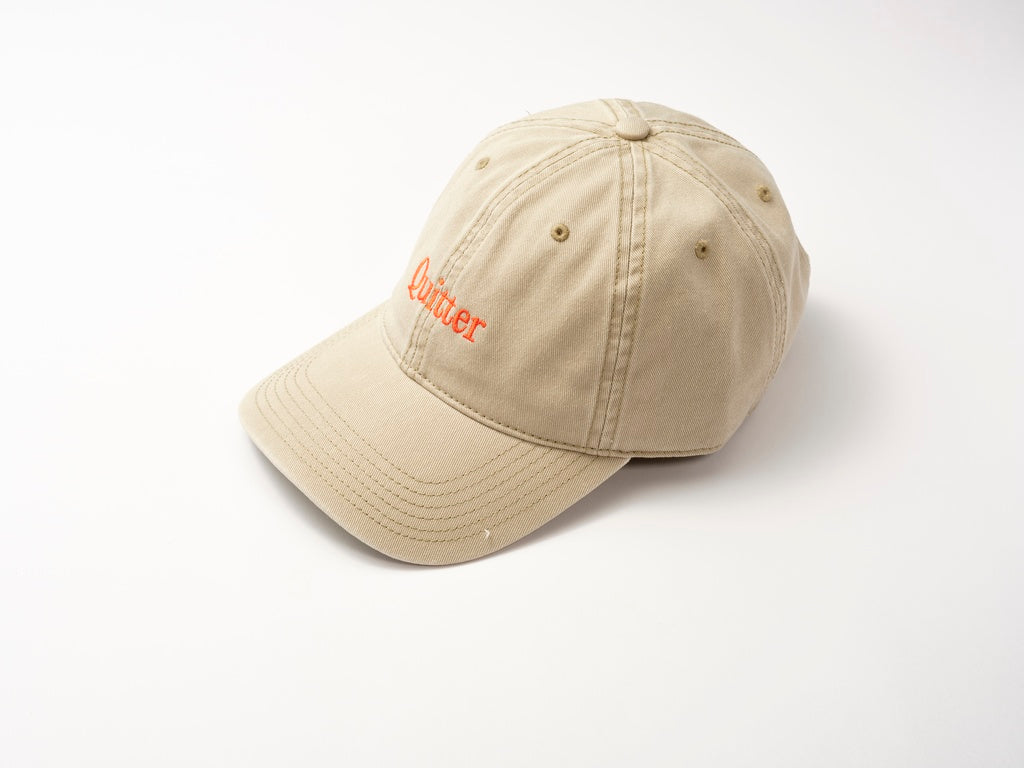 The Quitter Cap by Quit with Jones is a retro beige cotton twill baseball cap with bold red "Quitter" embroidery on the front, shown against a plain white background.