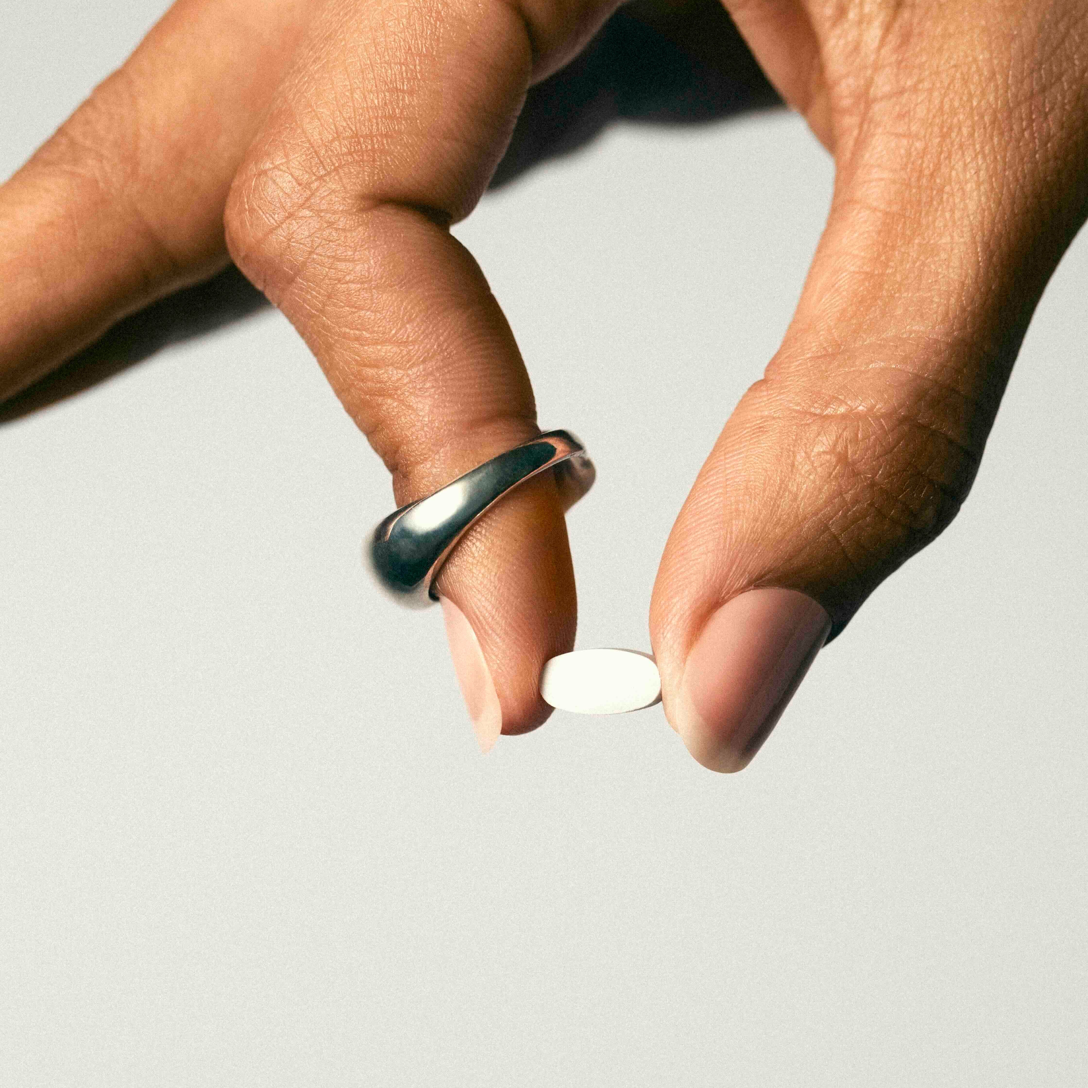 A hand holding a white Jones mini nicotine replacement therapy lozenge. FDA-approved nicotine mint for quitting vaping or quitting smoking.