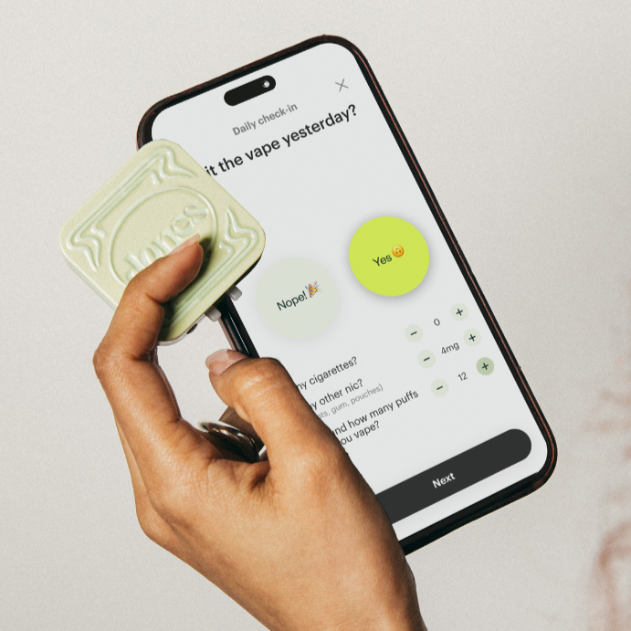 A hand holds a mint tactile token and a smartphone displaying the Jones App by Jones, featuring daily check-ins for quitting vaping with options "Nope!" (green) and "Yes" (yellow), plus prompts for usage details, supported by SMS coaching.
