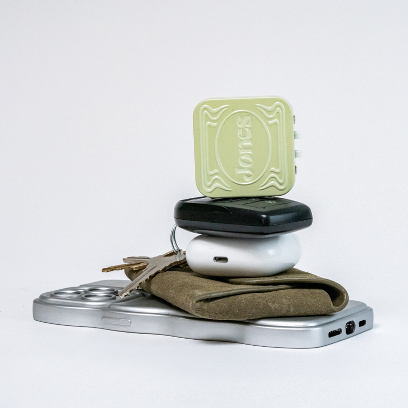 stack with phone, wallet, airpods case, keys and green jones tin