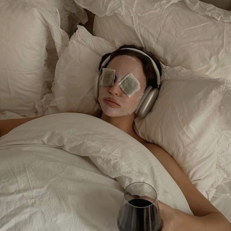 girl in bed with wineglass, eye mask and headphones