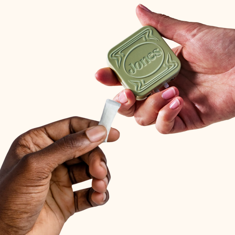 hand holding nicotine pouch and hand holding jones travel tin