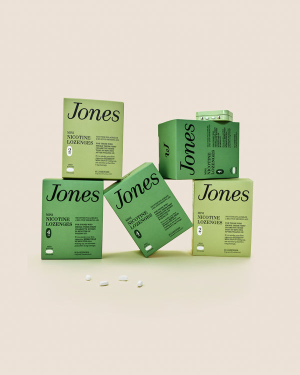 Five green boxes labeled "Jones Habit Kicker" are stacked geometrically on a beige background. Three white lozenges, part of this nicotine quit kit, are displayed in front. The boxes have minimalist text and icons.