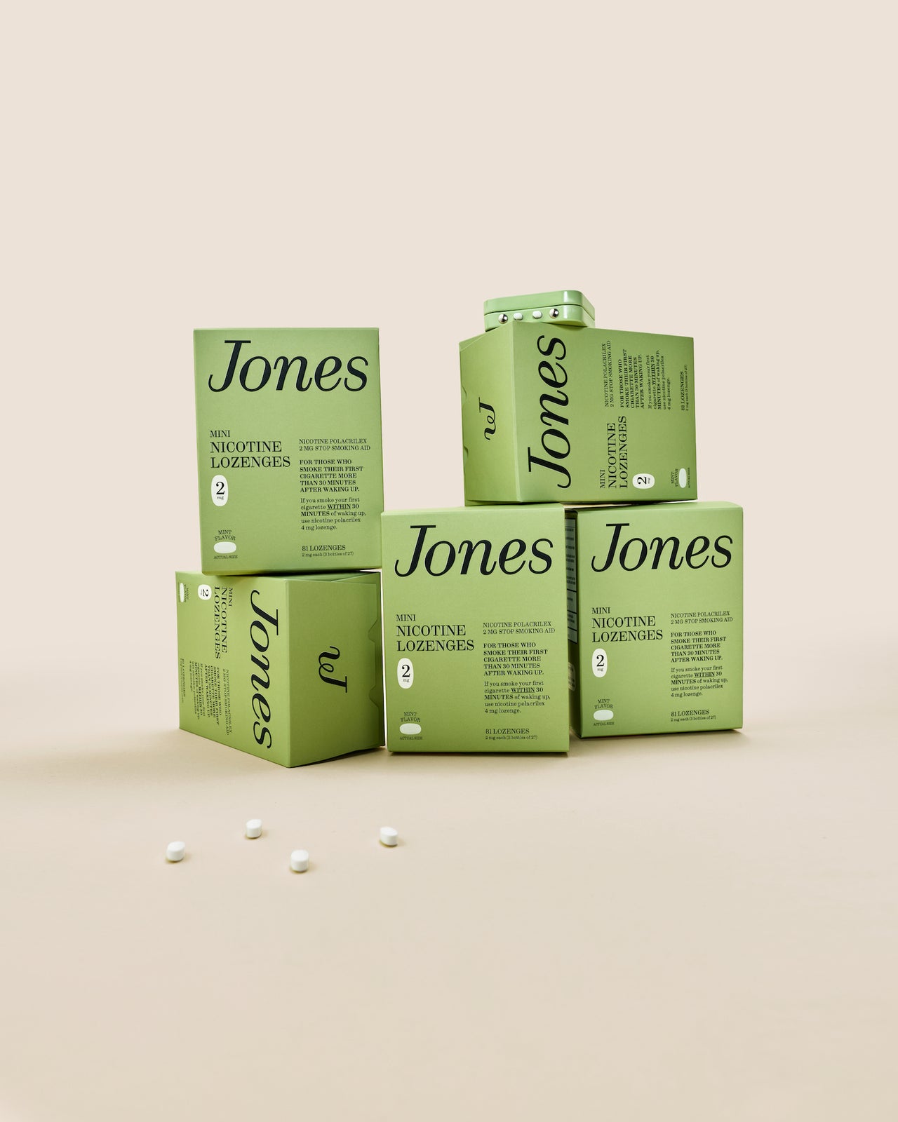 Five green boxes labeled "Jones Habit Kicker" are stacked geometrically on a beige background. Three white lozenges, part of this nicotine quit kit, are displayed in front. The boxes have minimalist text and icons.