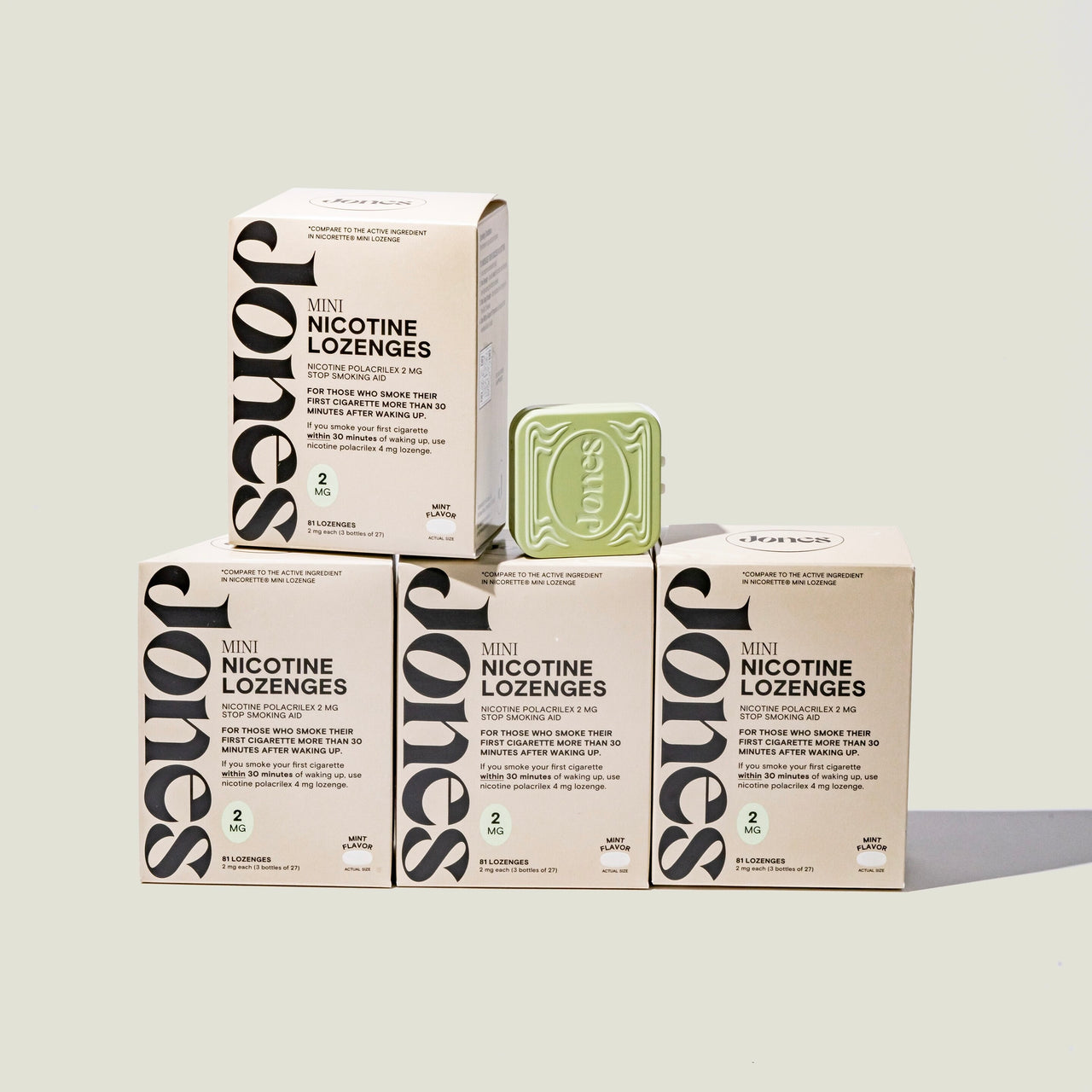 A beige box labeled “Quit with Jones 2mg Nicotine Mint” stands upright next to an open mint-green tin, both featuring minimalist packaging with dosage details, designed for nicotine replacement therapy on a plain white background.